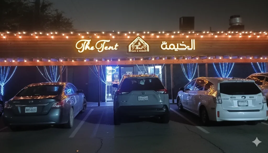 Festive "The Tent" restaurant with custom signs Houston, featuring Arabic text, lights, and parked cars at night.