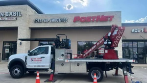 Professional truck with crane from a Houston sign company, parked outside a business strip with PostNet and Boba Tea signage.