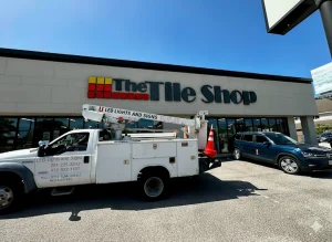 Houston sign installation crew using boom truck to mount The Tile Shop logo on building facade.
