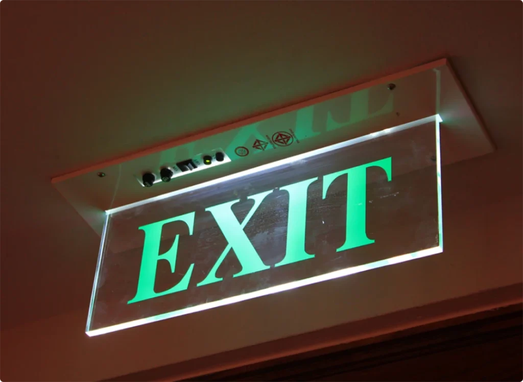 Bright green illuminated EXIT sign crafted by a sign manufacturer in Houston, mounted on the ceiling for clear visibility.