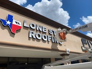 Worker installing a Lone Star Roofing sign with a Signage Company Houston, showcasing professional installation.
