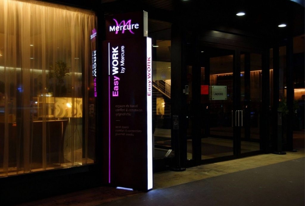 Illuminated outdoor totem sign manufactured in Houston for Mercure Easy Work by Mercure, featuring vibrant pink branding and white text on a dark background, professionally fabricated and installed by a Houston sign manufacturing company at night.