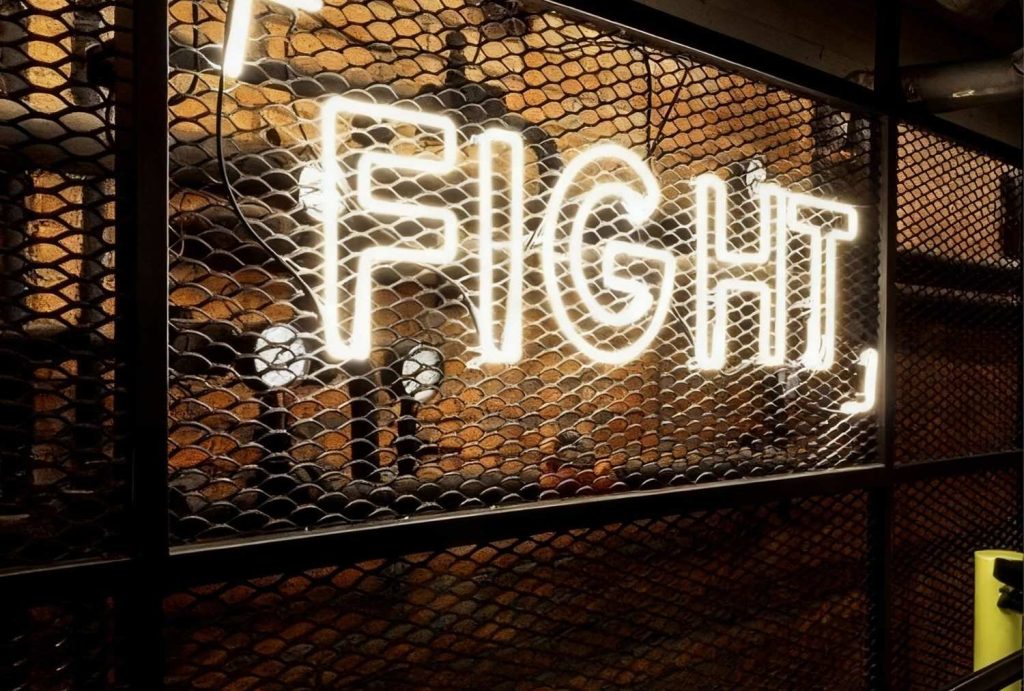 Bold custom neon "FIGHT" sign mounted behind metal grid – premium custom neon signs Houston