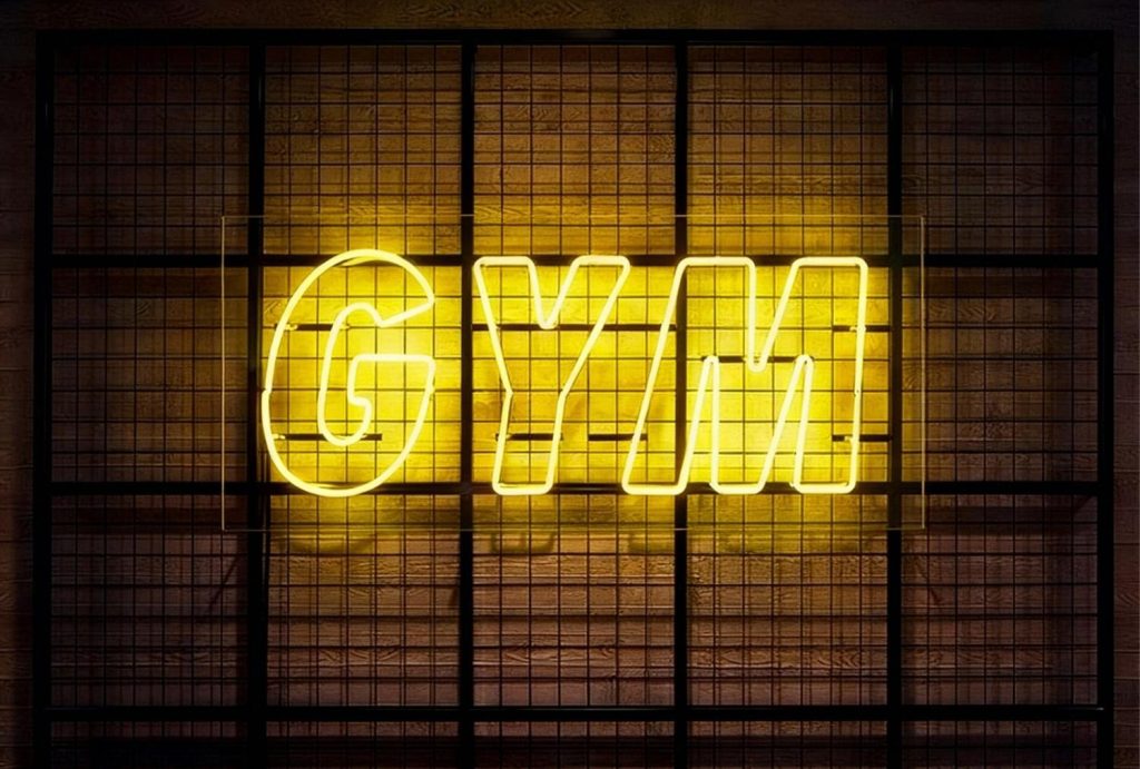 Bright yellow LED neon "GYM" sign on wooden wall with black grid – modern led neon business signs Houston