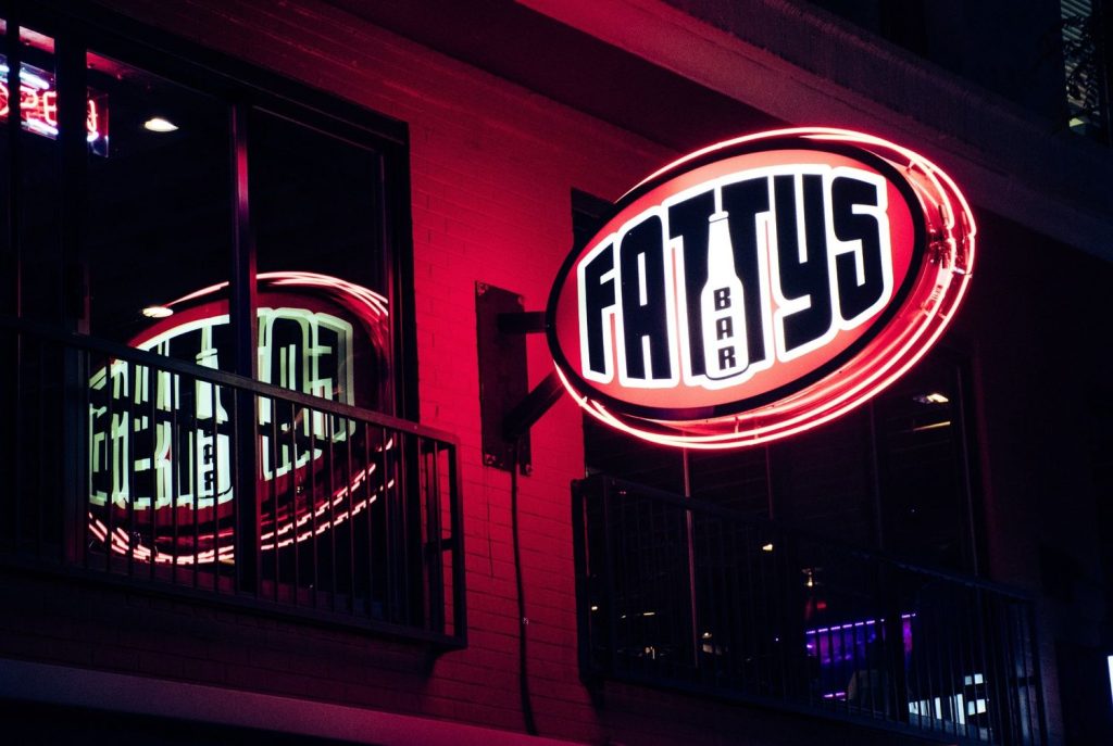 Oval-shaped Fatty's Bar neon outdoor signs for businesses Houston, illuminated in bright red on a brick building.