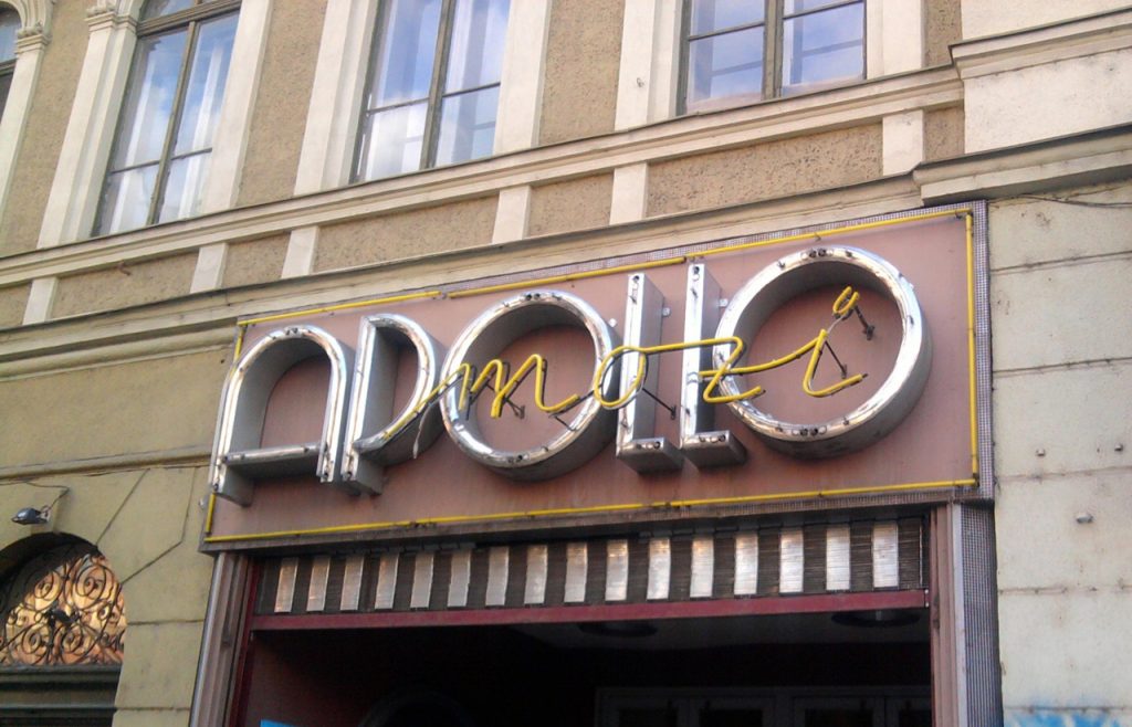 Retro Apollo cinema building signs Houston featuring yellow neon tubes and silver channel letters on a stone facade.