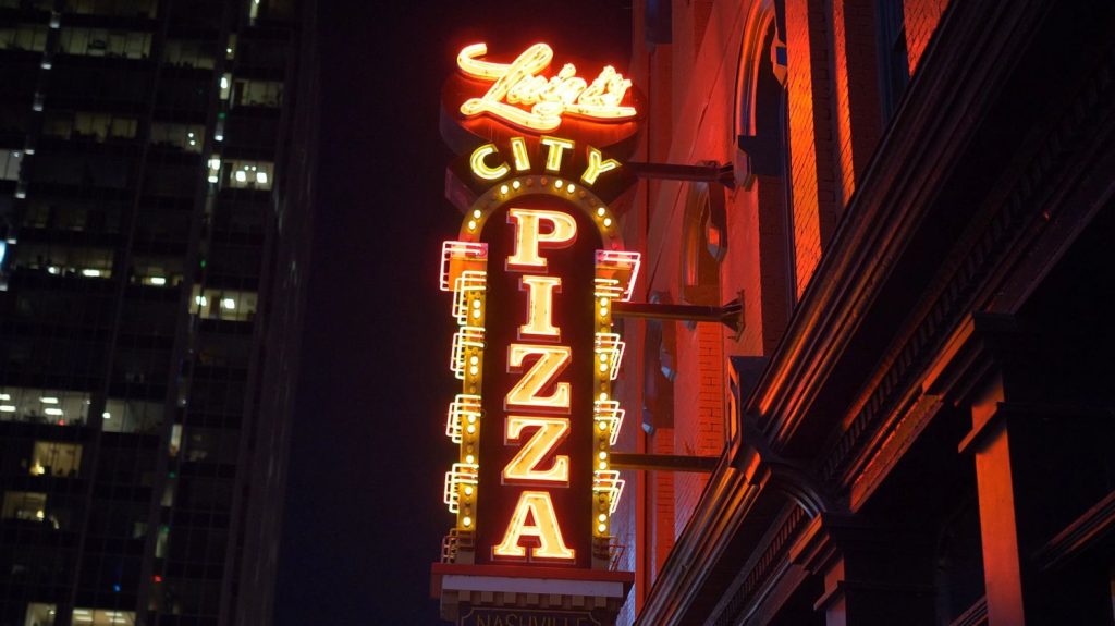 Vintage Luigi’s City Pizza neon business signs Houston style glowing at night with red and yellow lights on a building.