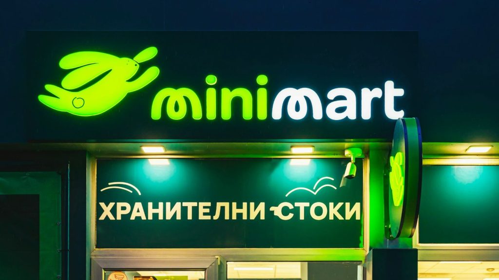 Glowing green neon minimart office signs with a rabbit logo and Cyrillic text displayed on a modern storefront.