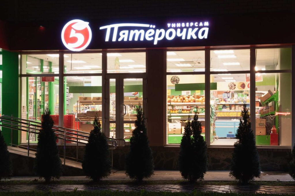 Illuminated retail office signs above a Pyaterochka grocery store entrance with bright white and red lettering.
